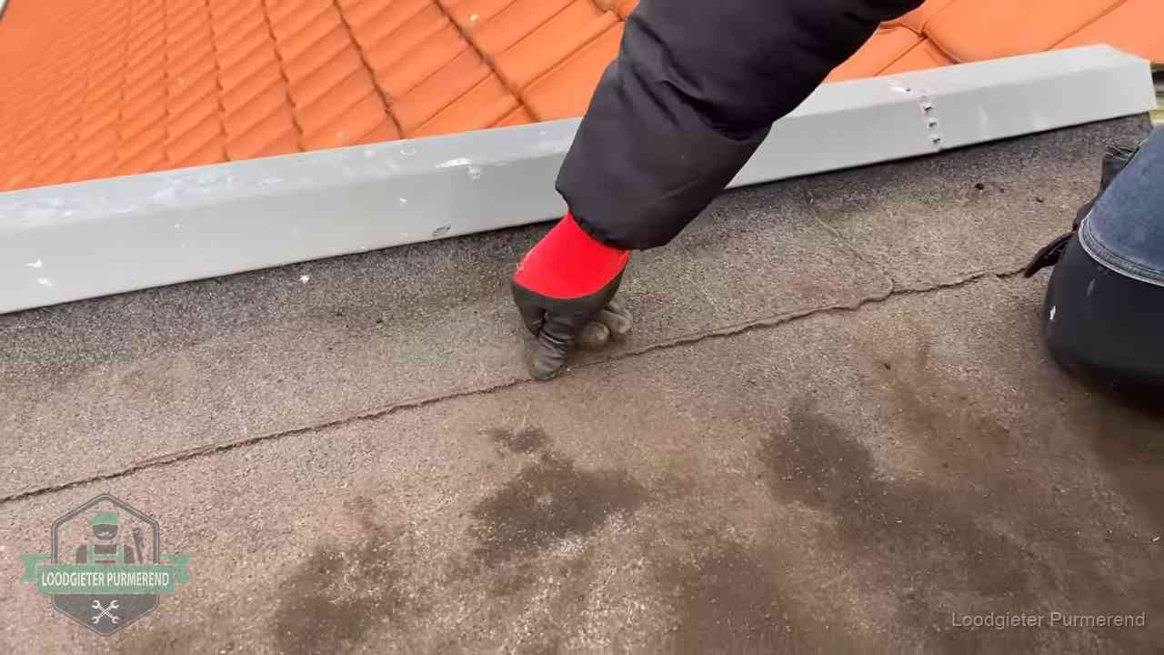 Vakman wijst een naad met vochtplekken aan op een bitumen plat dak in Purmerend