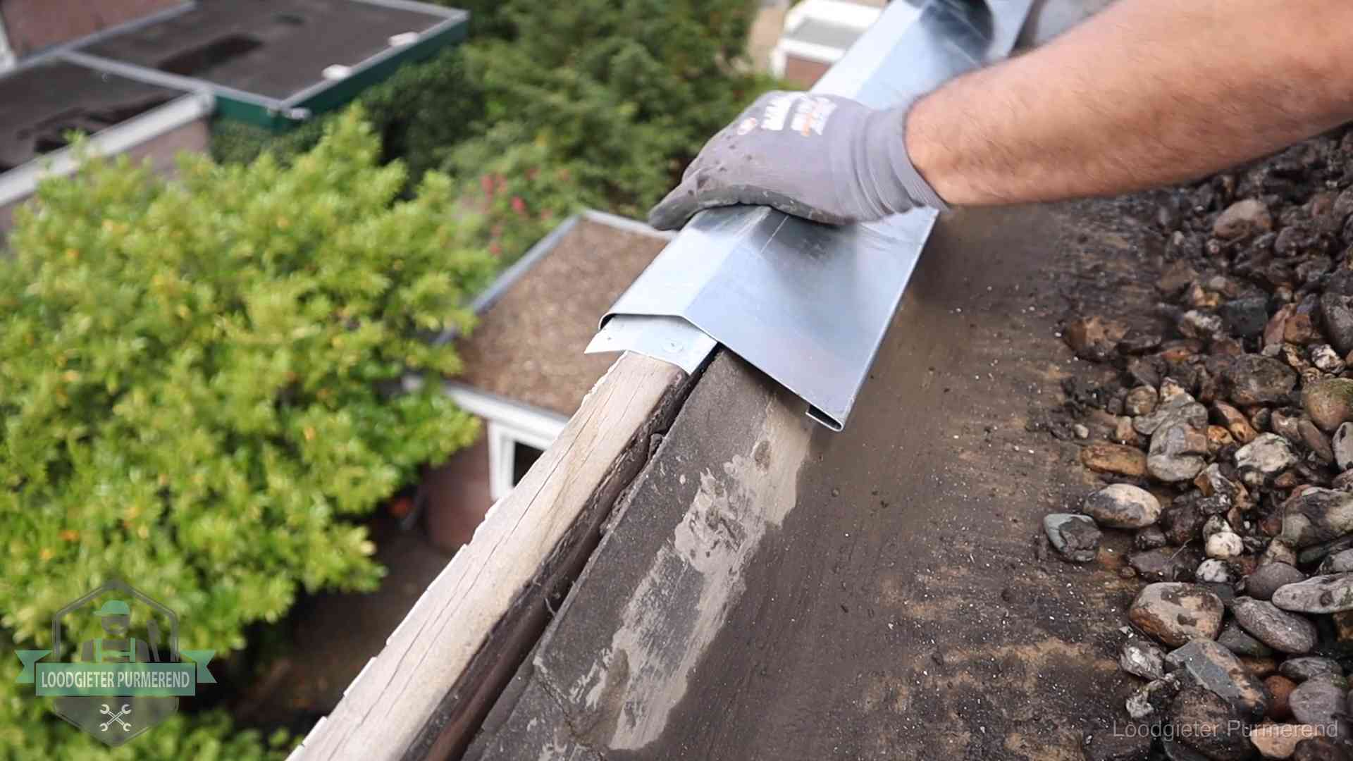 Dakdekker plaatst een zinken deklijst op een dakrand met uitzicht over een woonwijk in Purmerend