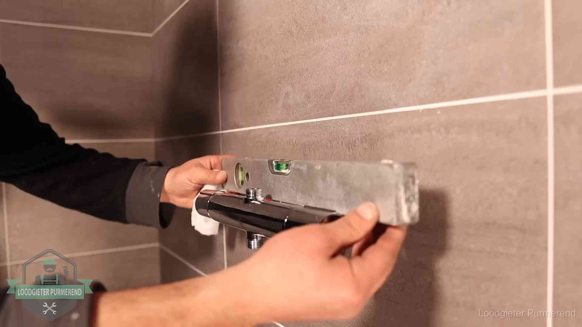 Loodgieter lijnt een douchekraan uit met een waterpas in een woning in Purmerend