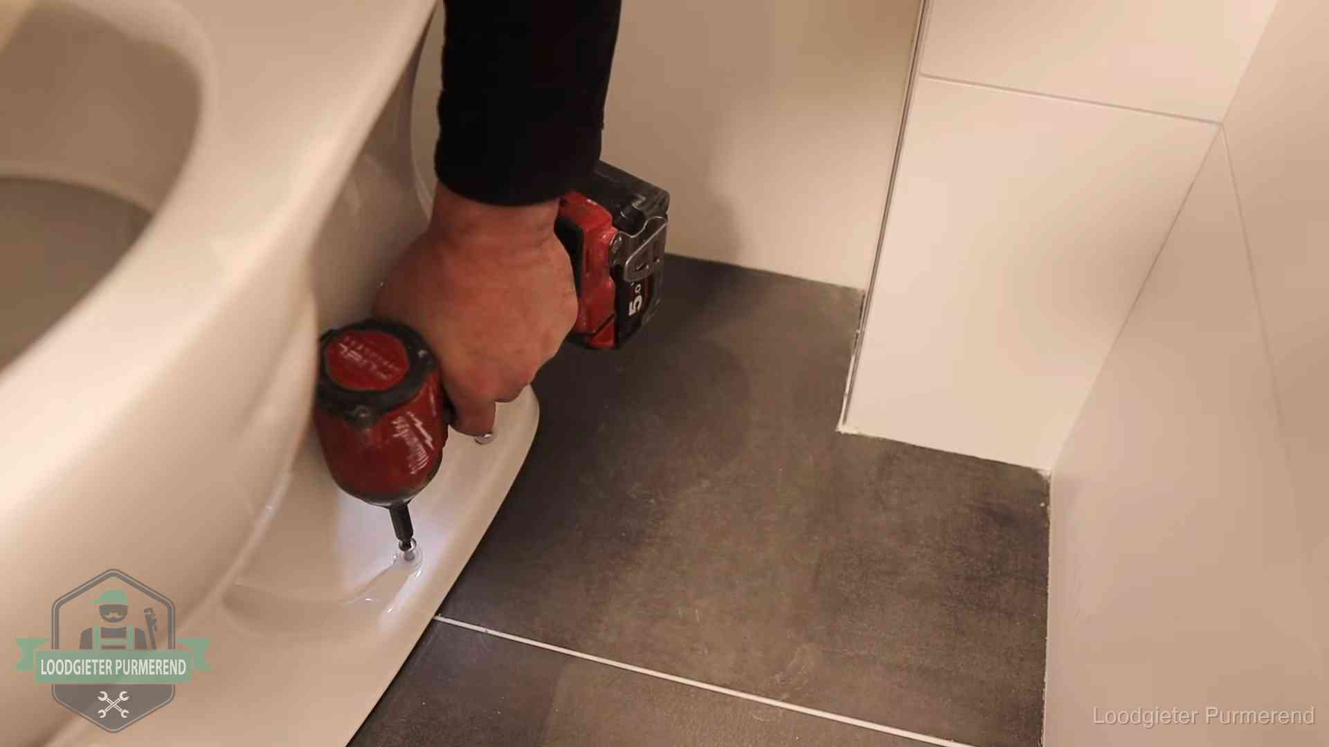 Kosten wc ontstoppen in Purmerend Loodgieter zet de voet van een wc-pot vast op de tegelvloer in Purmerend